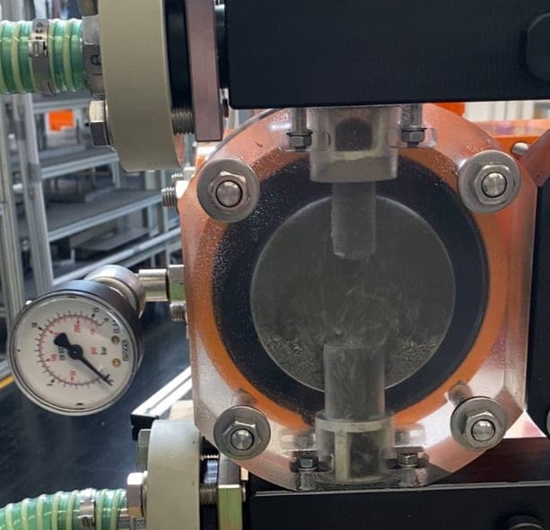 Transparenter Pumpenkopf im Versuchsaufbau, gefüllt mit abrasivem Strahlmittel